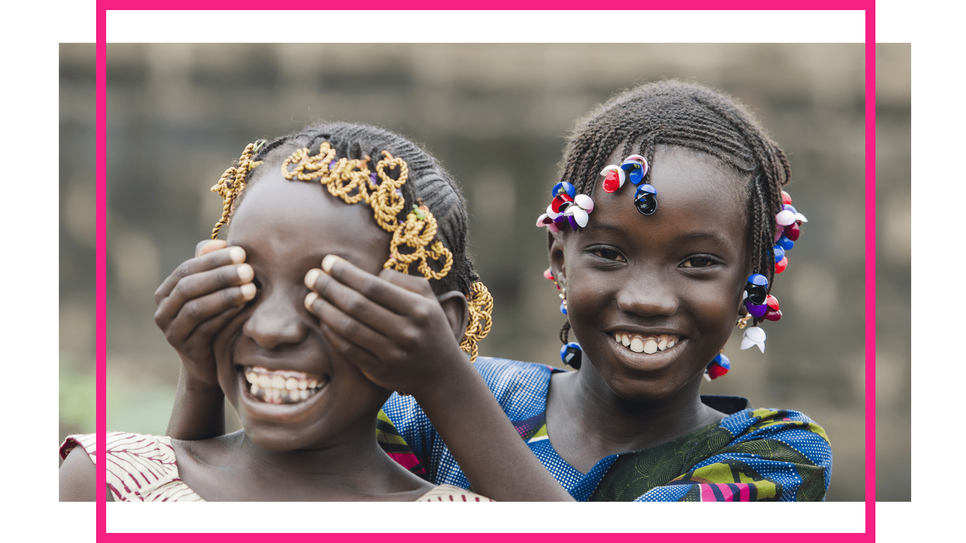 Two African girls smiling, one covering the other's eyes