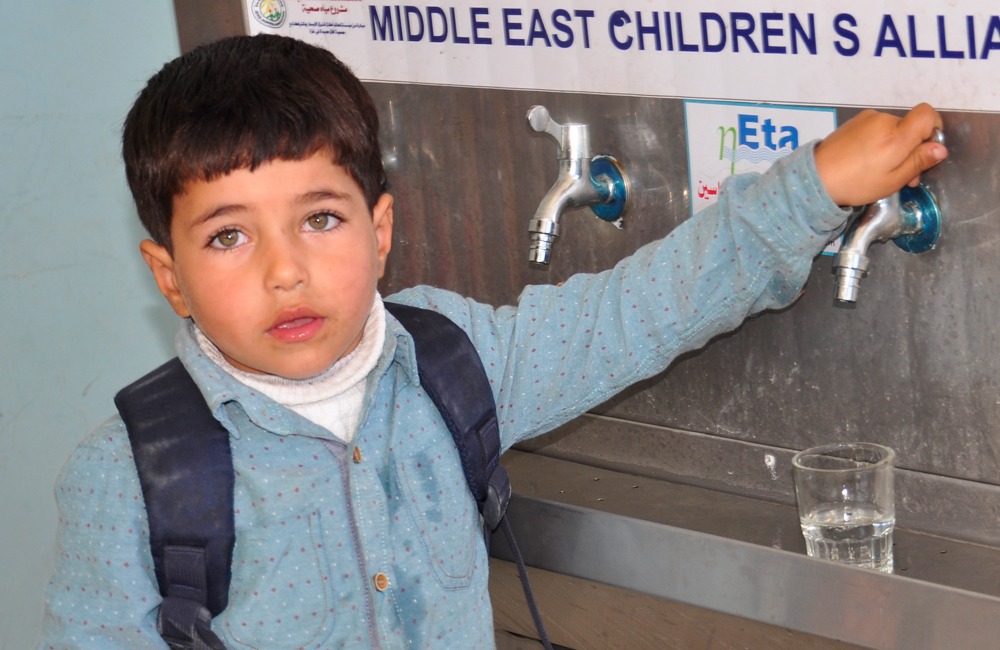 Little boy opening water faucet in a school in Gaza