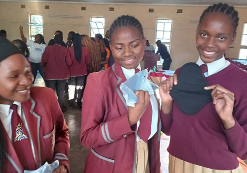 Three Zimbabwean students in their school uniform show period pads the've been given at a period hygiene workshop
